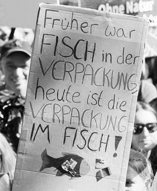 Demonstrationsplakat mit der Aufschrift „Früher war Fisch in der Verpackung, heute ist die Verpackung im Fisch!“ vor einer Menschenmenge